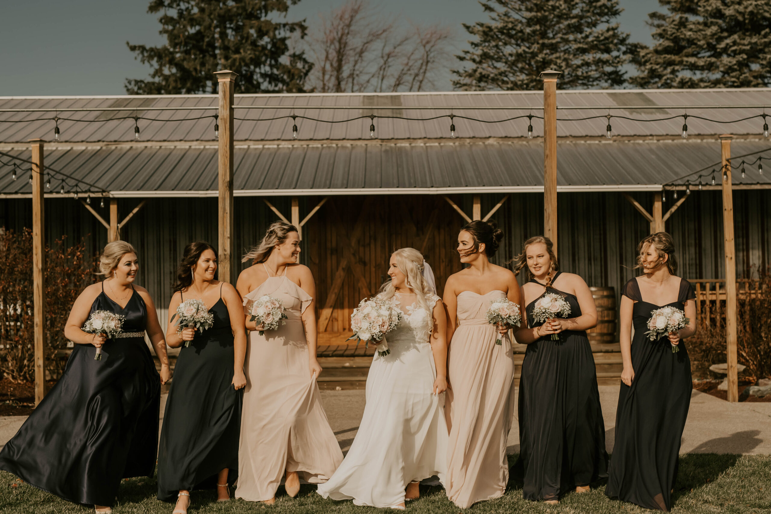 bride walks with her bridesmaids in front of a barn at her Michigan barn wedding venue