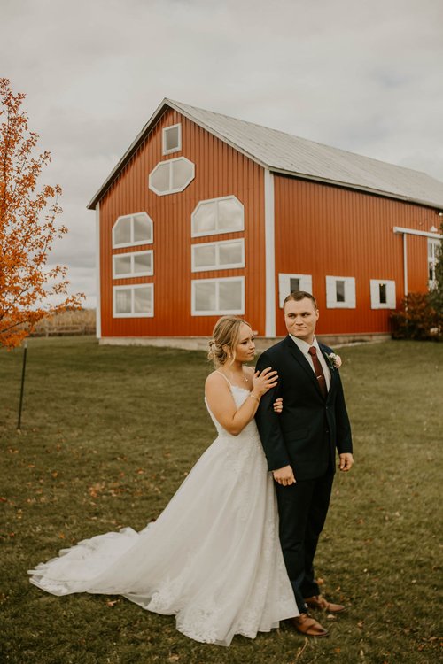 bride and groom take photos in front of red barn